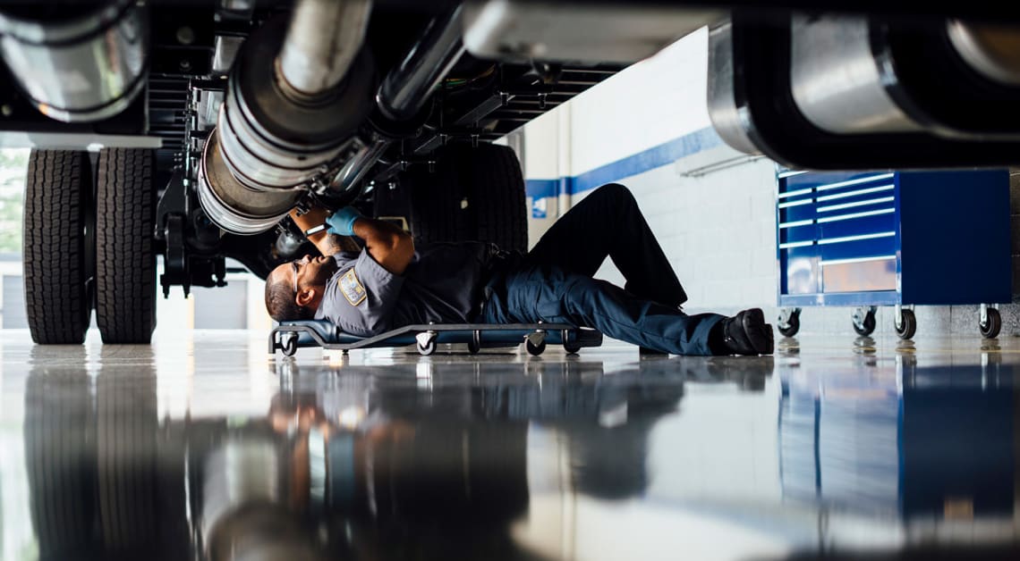 A mechanic fixing a truck engine under the hood.